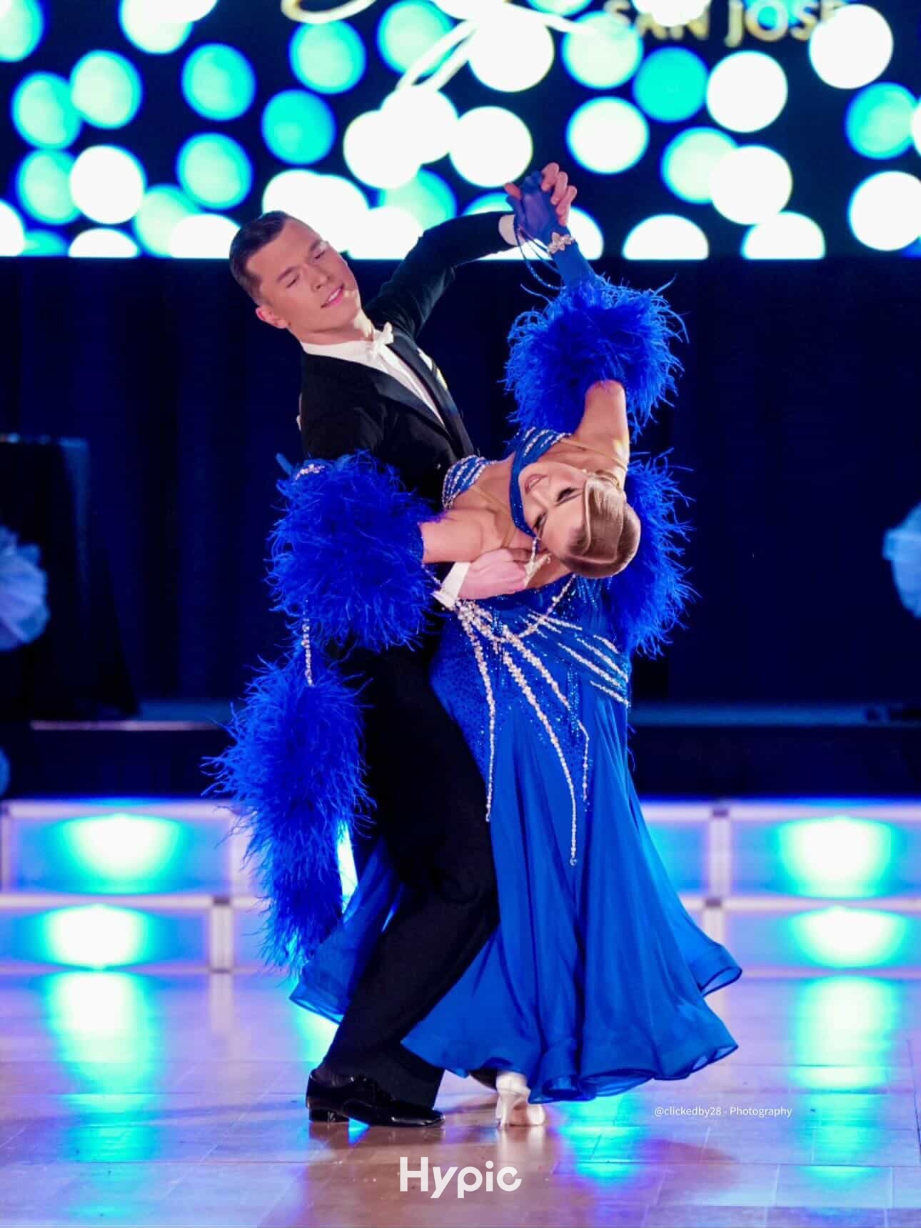 Professional couple performing in a blue feathered competition gown on stage